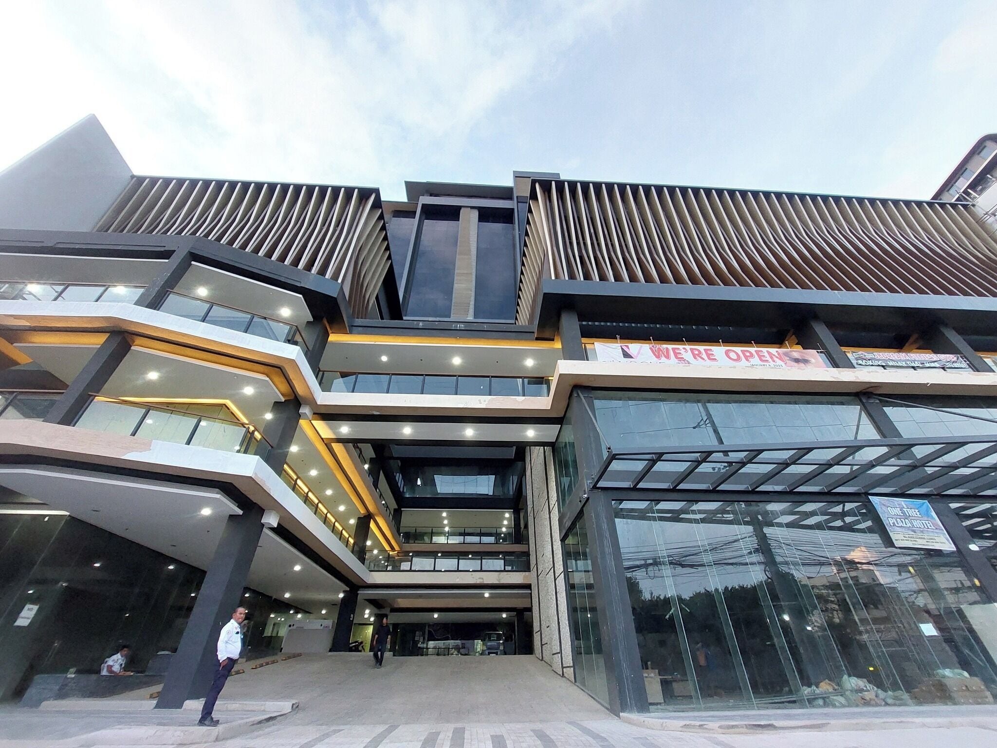 A modern multi-story building with a glass facade, multiple levels, and a sign indicating the business is open.