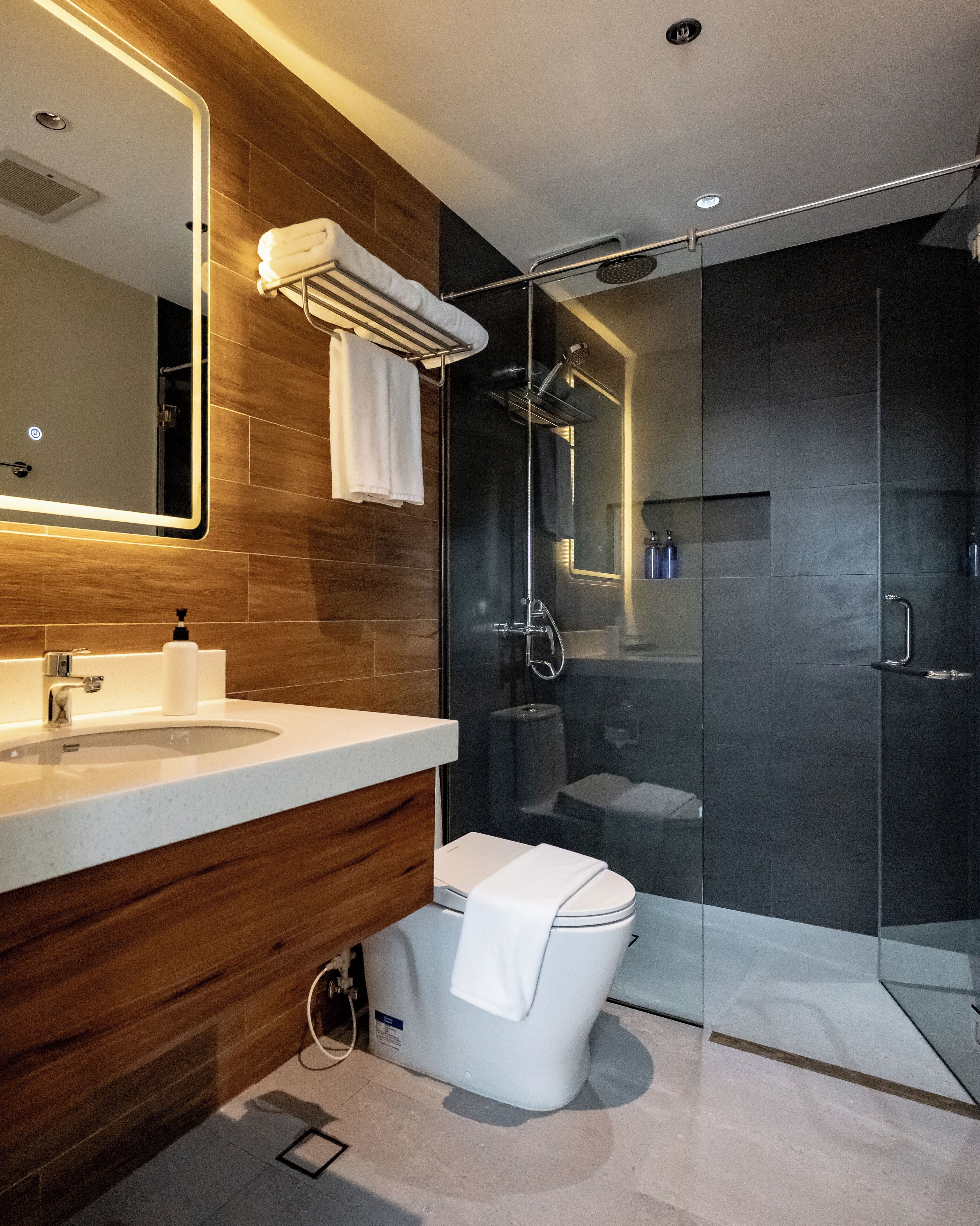 Un baño moderno con un tocador de madera, cabina de ducha de vidrio y un inodoro.