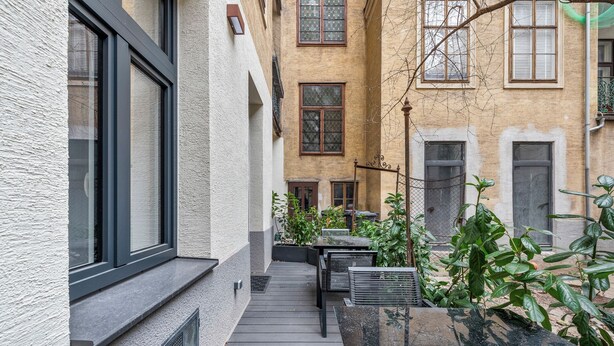 A narrow courtyard with a wooden deck, potted plants, and a metal fence. - easy-flat Votiv - 153sqm Apartment with Terrace (Vienna)