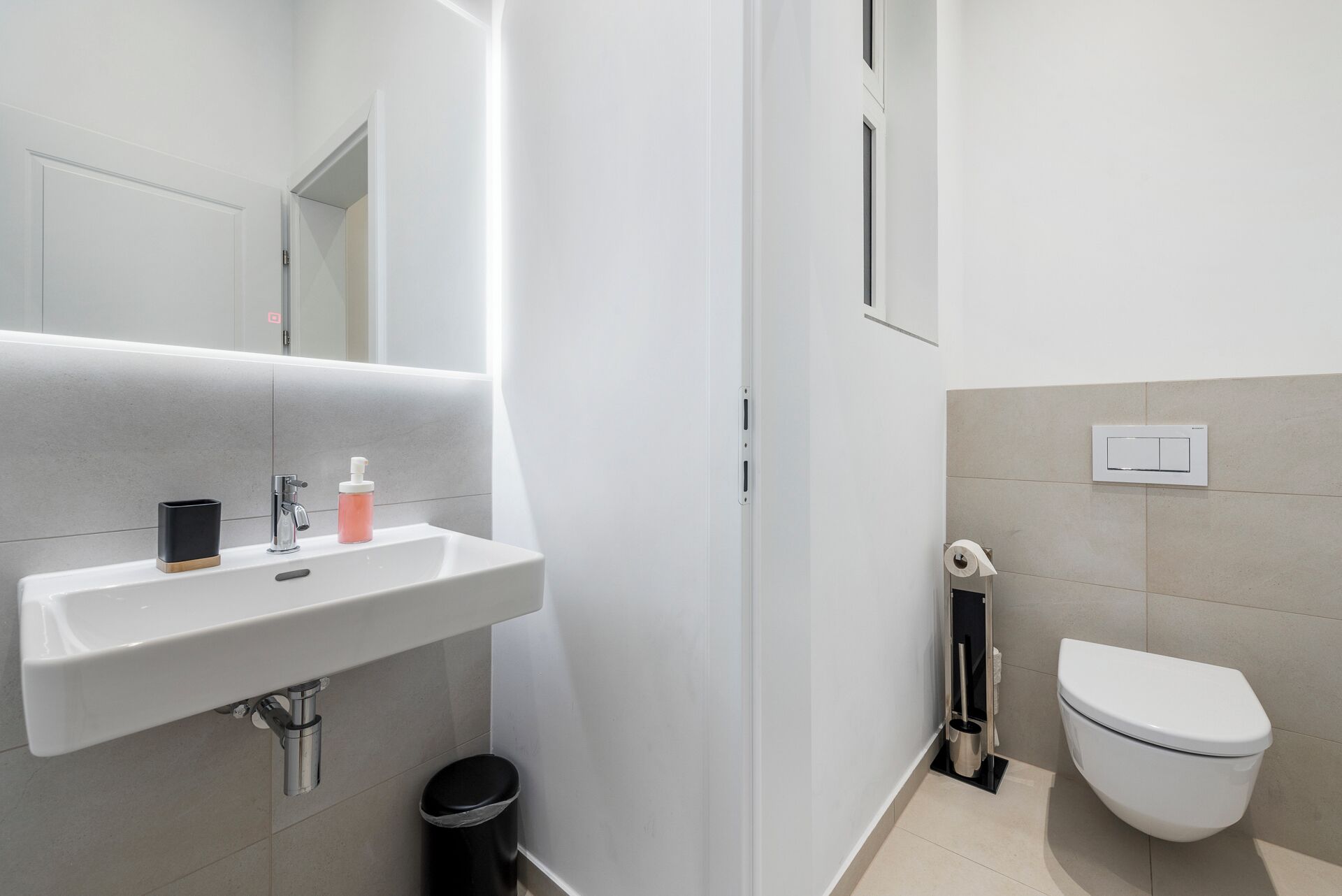Un baño moderno con lavamanos, espejo e inodoro blancos.