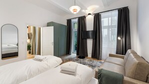A modern hotel room with two beds, a sofa, a TV, and a large window with curtains. - easy-flat Votiv - 153sqm Apartment with Terrace (Vienna)