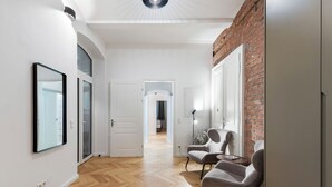 A modern hallway with wooden flooring, white walls, and a brick accent wall. There are two armchairs and a small table with a lamp. - easy-flat Votiv - 153sqm Apartment with Terrace (Vienna)