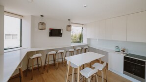 Une cuisine moderne avec des meubles blancs, un four encastré et un coin repas équipé de tabourets.