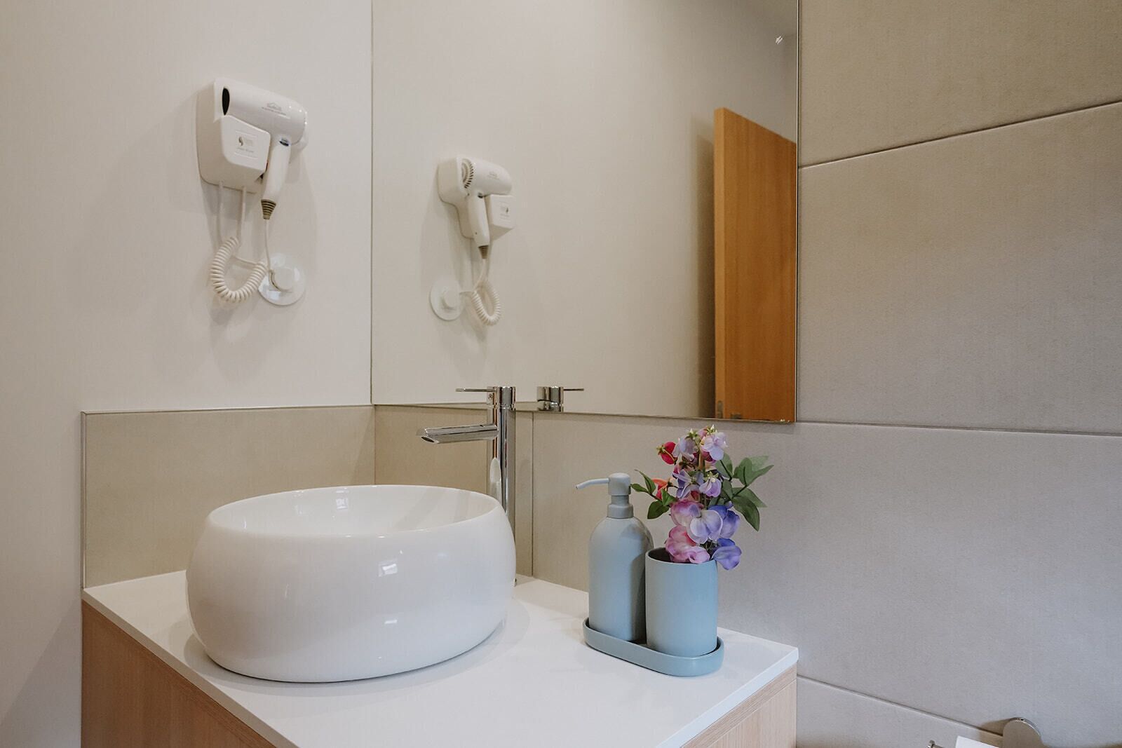 Un baño moderno con un lavabo blanco grande, un espejo y dos secadores de pelo montados en la pared.