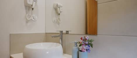 Un baño moderno con un lavabo blanco grande, un espejo y dos secadores de pelo montados en la pared.