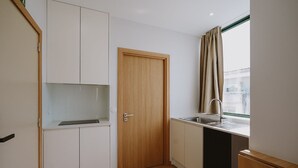 Une cuisine de taille réduite avec une porte en bois, des placards blancs, une fenêtre avec des rideaux et un évier.