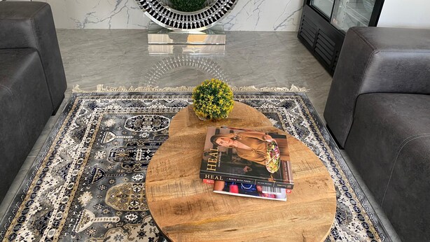 Un salon moderne avec un mur en marbre, une étagère décorative en métal, un tapis à motifs et deux canapés en cuir.