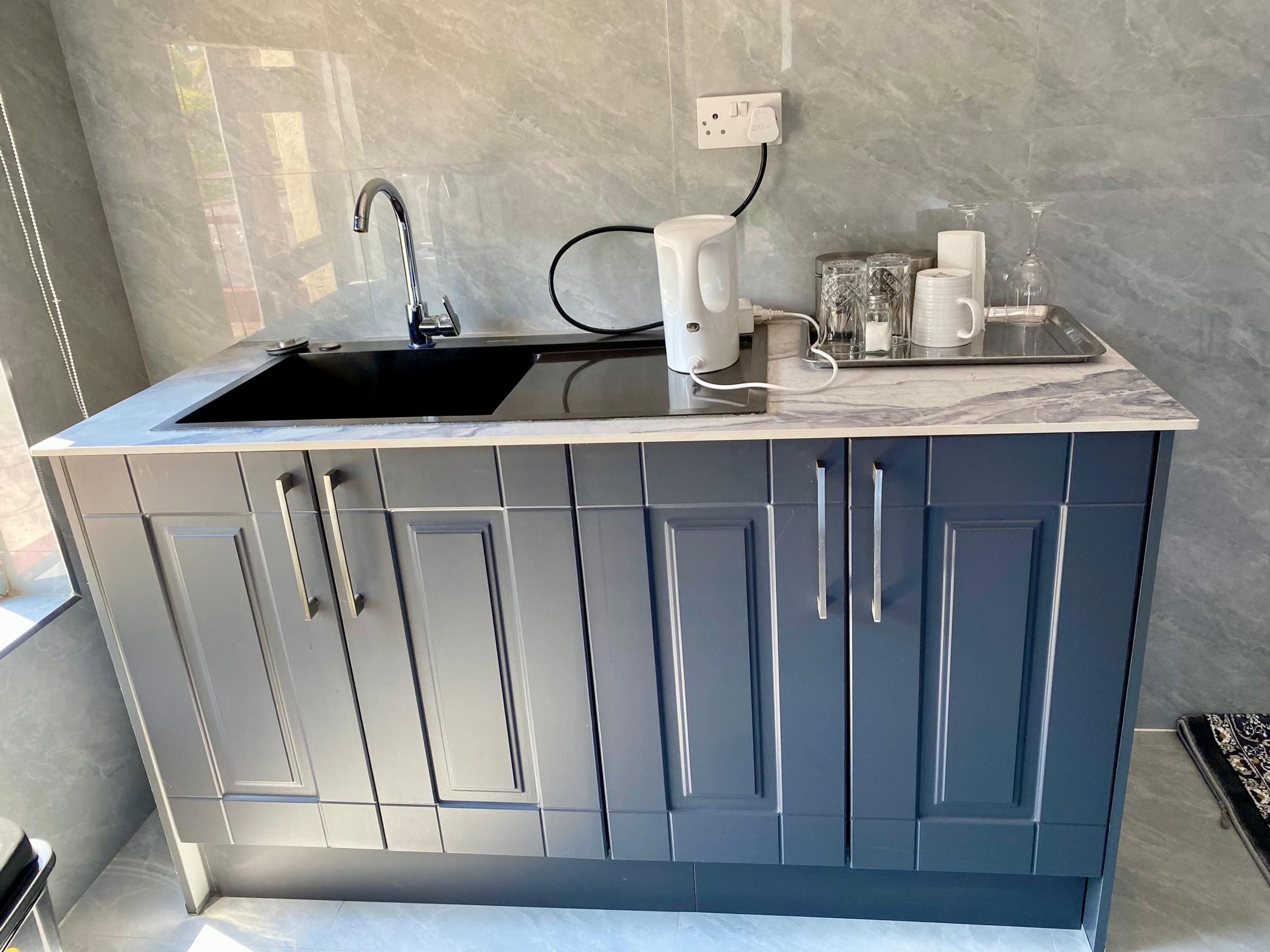 Una cucina moderna con lavello nero, mobili grigi e piano di lavoro in marmo.