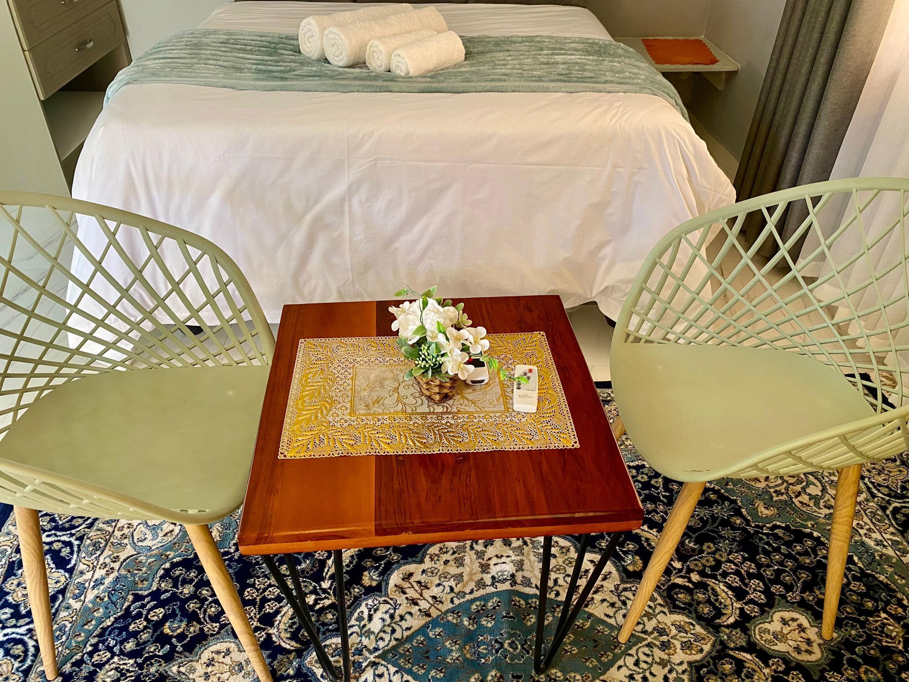 A hotel room with a bed, two chairs, a small table with a placemat, and a vase with flowers.