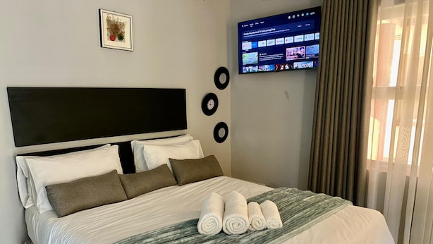 Una cama bien hecha con ropa de cama blanca y gris, un plaid gris a rayas y toallas enrolladas.