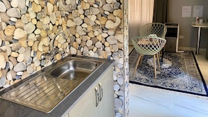 Una cocina con salpicadero de pared de piedra, un lavamanos de acero inoxidable y una silla moderna.