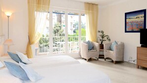 A bedroom with two beds, a balcony, wicker chairs, a TV, and a painting. - Spacious Studio Apartment Close to The Martinez - 2313 (Cannes)