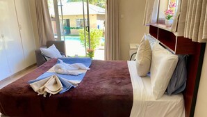 A hotel room with a large bed, a chair, and a view of the outside. - Poolside Executive Suite Near Airport - 2322 (Harare)