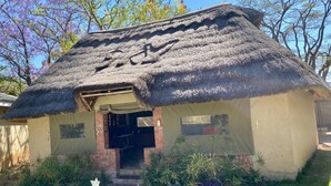 A thatched-roof building with a brick entrance and a small porch area. - Poolside Executive Suite Near Airport - 2322 (Harare)