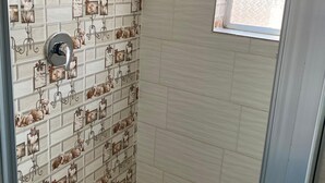 Doccia con parete piastrellata decorata con motivi canini e floreali, soffione metallico e finestra vista esterna.