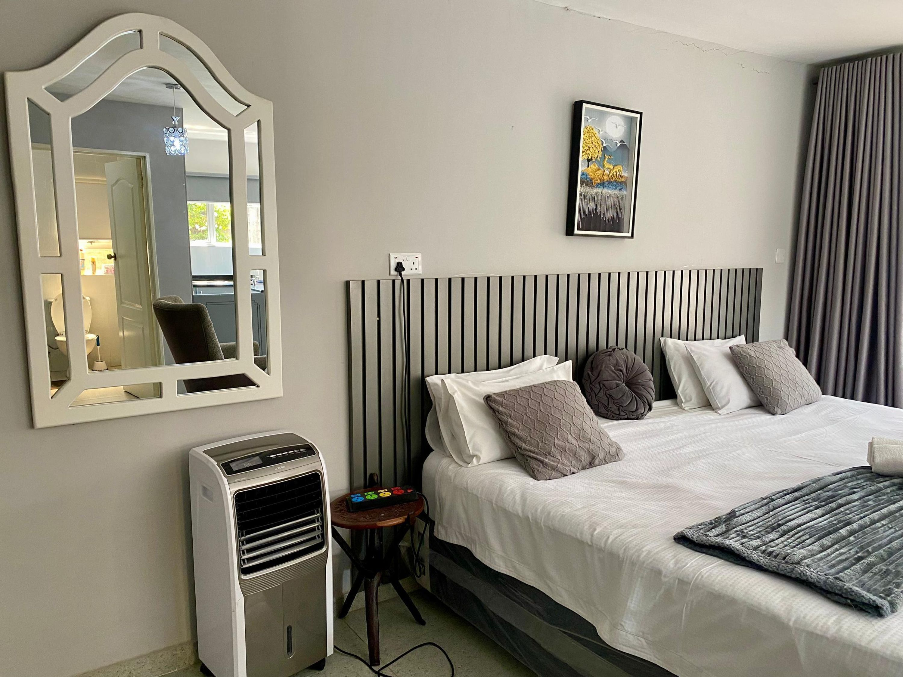 A hotel room with a bed, a mirror, a heater, and a picture on the wall.