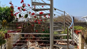 Una escala de caragol amb barana metàl·lica, envoltada d'un jardí ple de flors vermelles i vegetació.
