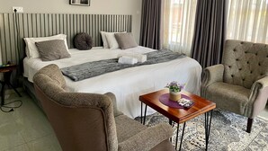Habitació d'hotel amb un llit, dues butaques, una taula petita amb un ram i un quadre al mur.