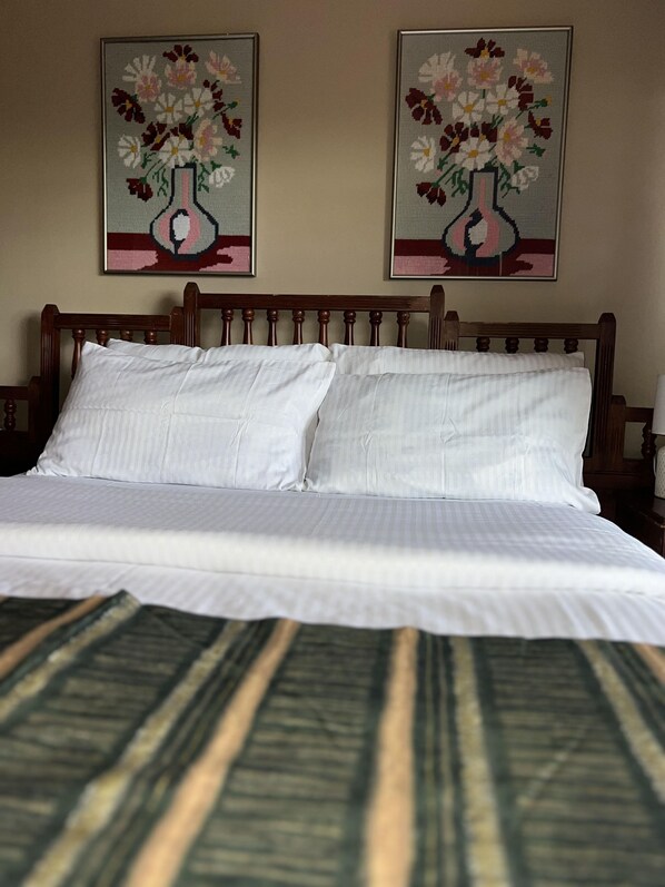 A neatly made bed with white linens and a striped bedspread. There are two framed floral paintings on the wall above the bed.