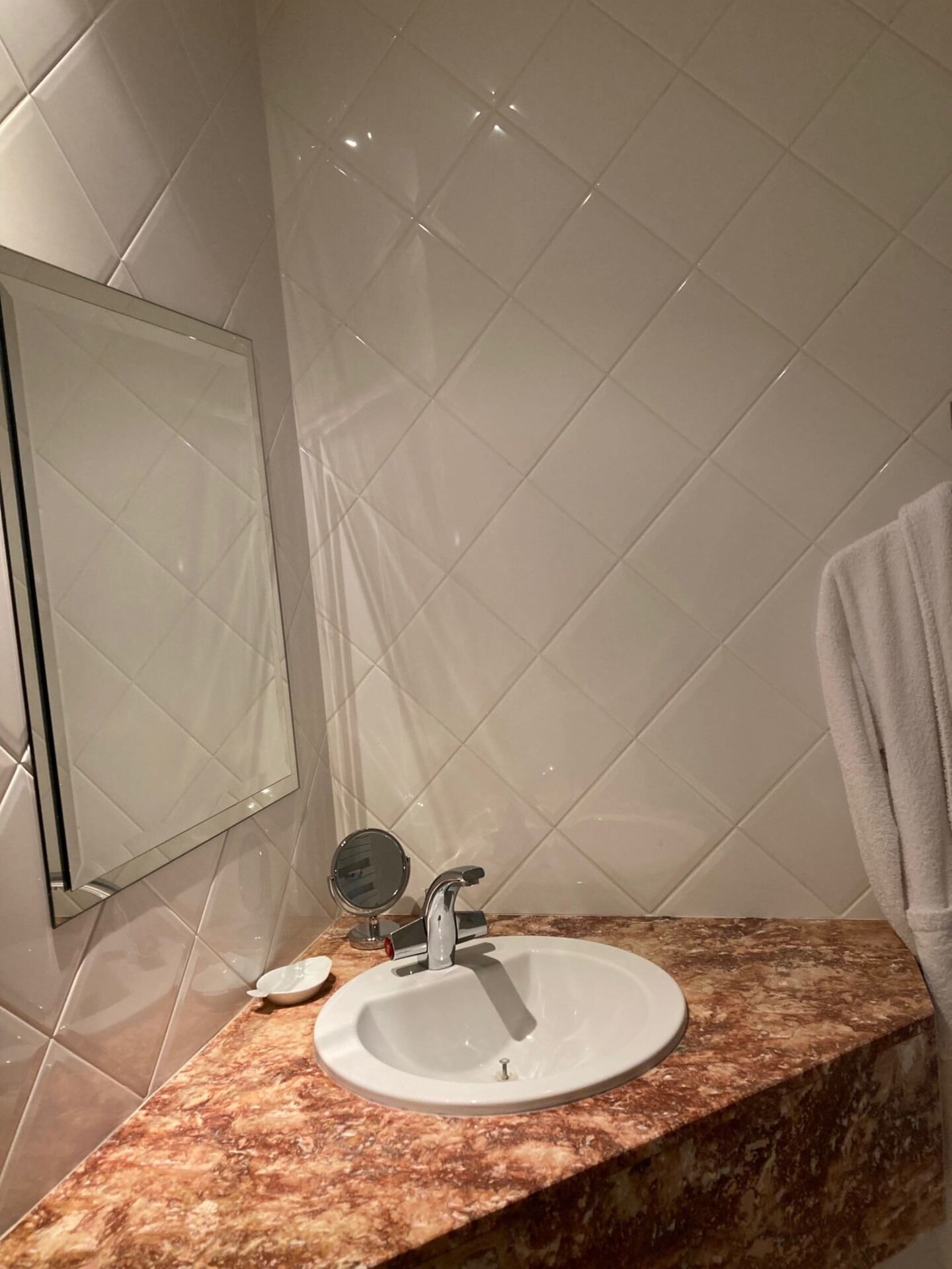 Un baño con encimera de mármol, lavamanos, espejo y perchero.