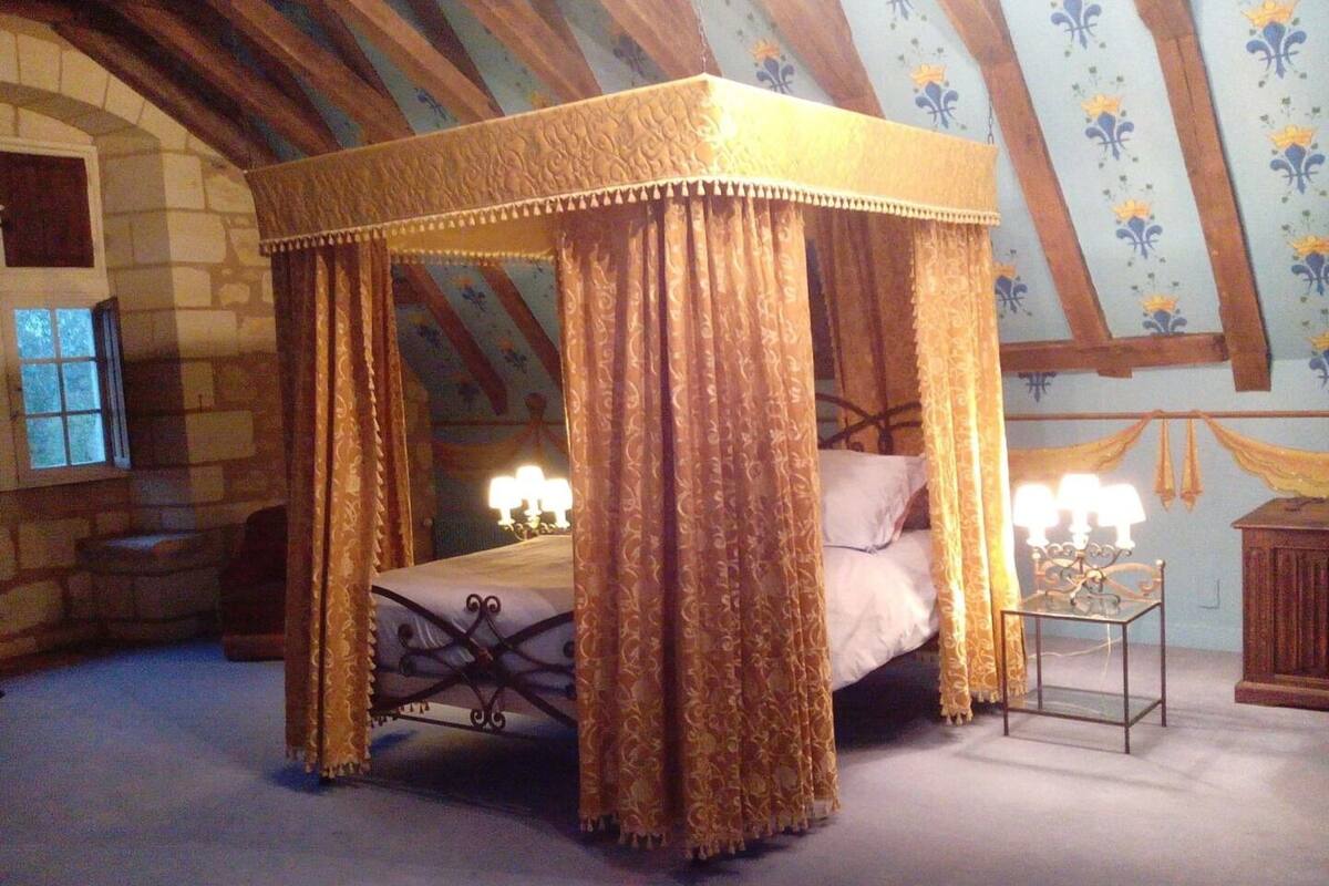 Un lit à baldaquin à quatre poteaux avec des rideaux, une table de chevet avec des lampes et un mur en pierre avec une fenêtre.