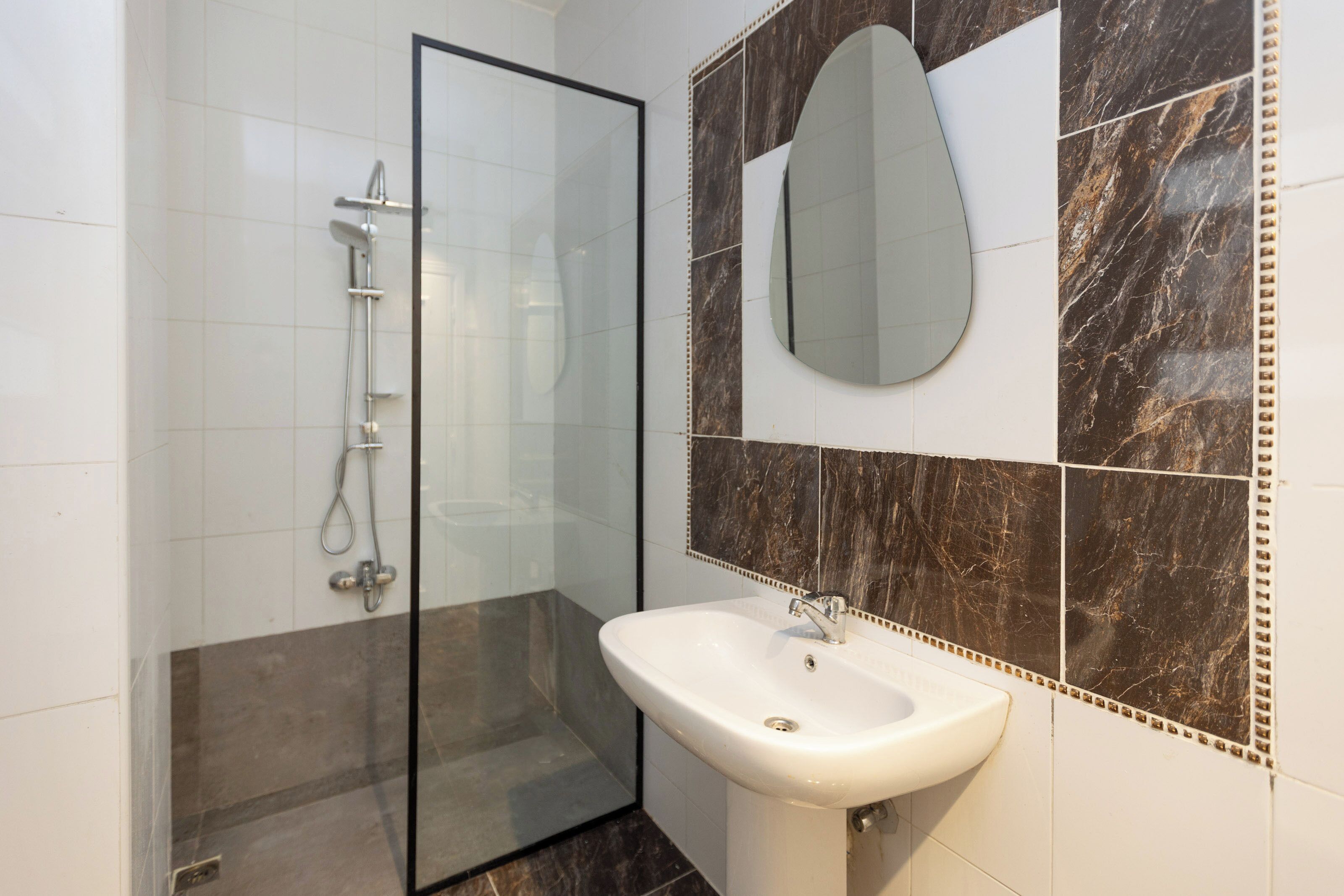 A modern bathroom with a glass shower enclosure, a white sink, and marble tiles.