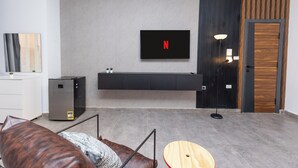 A modern living room with a flat-screen TV mounted on the wall, a built-in entertainment unit below it, a sofa, a coffee table, and a door with a wooden panel design. - Host Prime Boutique hotel 04 (New Cairo)