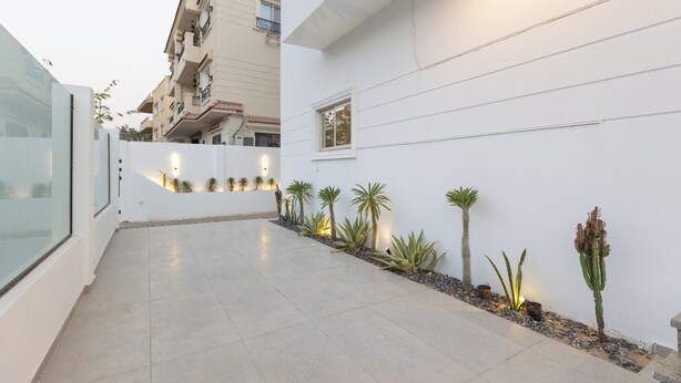 A modern building with a clean, white exterior, a tiled patio, and small potted plants along the wall. - Host Prime Boutique hotel 04 (New Cairo)