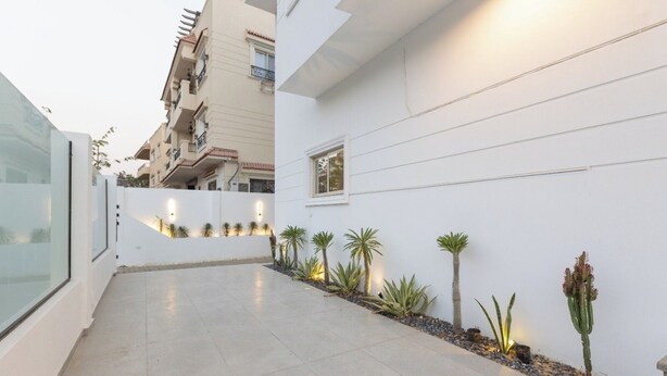 A modern building with a clean, white facade, a tiled patio, and small potted plants along the wall. - Host Prime Boutique Hotel 01 (Shurtah al-Dakhlah)