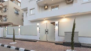 A modern residential building with a gated entrance, a small garden area with white pebbles, and a tall coniferous tree. - Host Prime Boutique Hotel 01 (Shurtah al-Dakhlah)