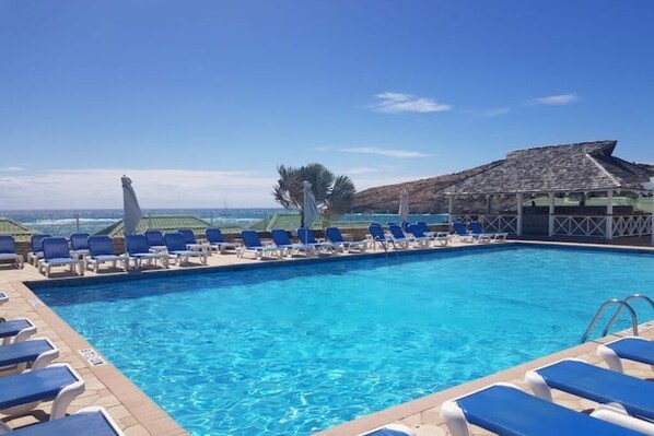 A swimming pool with blue lounge chairs and a view of the ocean. - Beautiful Beach Front Villa in a prime location (Saint Paul's)