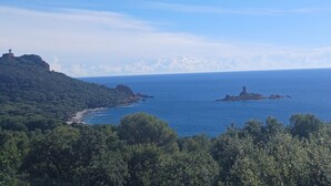 A coastal landscape with a lighthouse on a hill, a beach, and a small island with a tower. - Exceptional sea view Quiet, swimming pool and nature 20 minutes from Cannes (Saint-Raphaël)