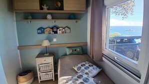 A compact bedroom with a bed, a nightstand, a window with a view, and a shelf with decorative items. - Exceptional sea view Quiet, swimming pool and nature 20 minutes from Cannes (Saint-Raphaël)