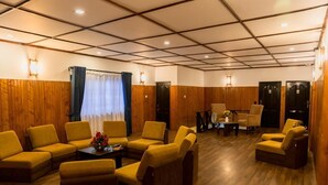 A hotel lobby with wooden paneling, yellow armchairs, a coffee table with flowers, and a small table with a vase. - Nat City Hotel Nuwaraeliya (Nuwaraeliya)