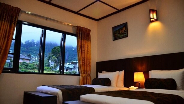 A hotel room with two beds, a large window with curtains, a nightstand with a lamp, and a painting on the wall. - Nat City Hotel Nuwaraeliya (Nuwaraeliya)