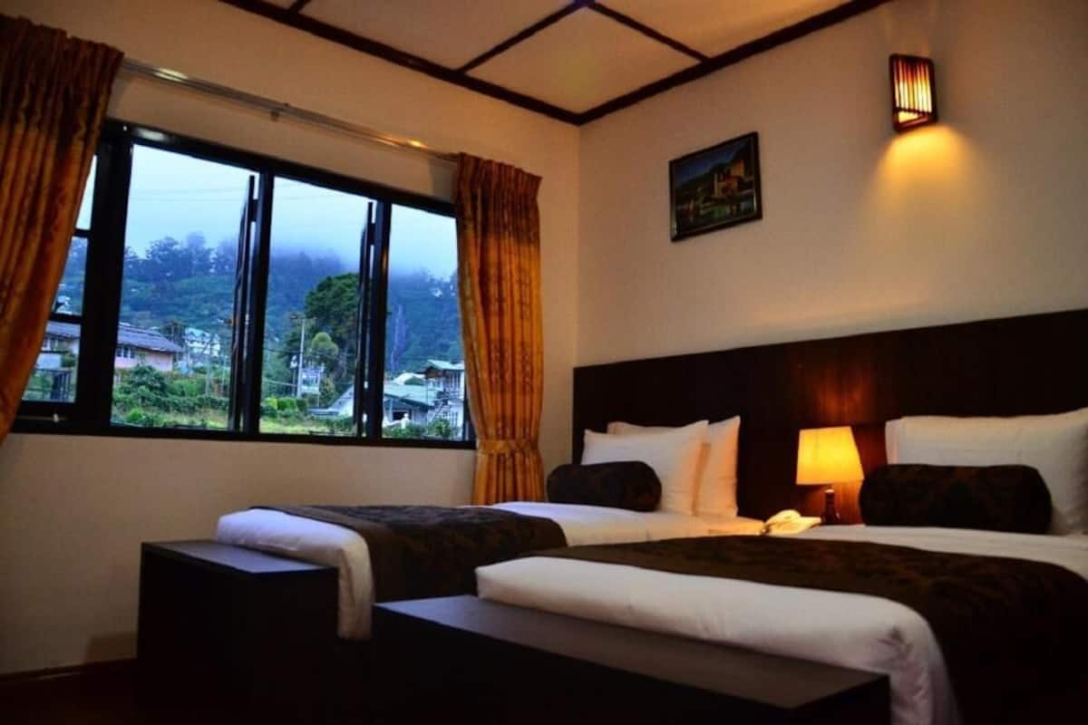 A hotel room with two beds, a large window with curtains, a nightstand with a lamp, and a painting on the wall.