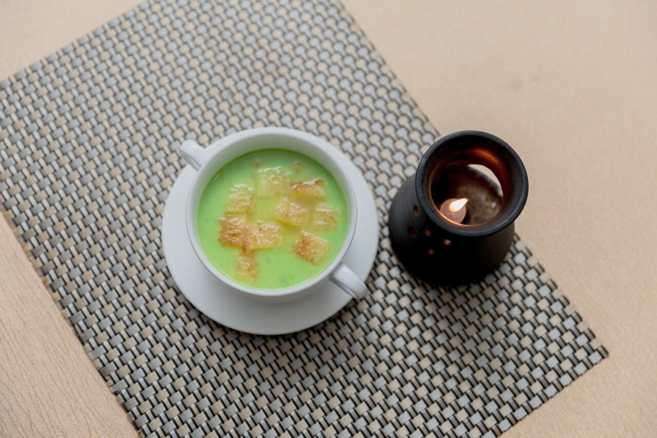 Eine weiße Tasse grüne Suppe mit Croutons auf einer gewebten Unterlage.