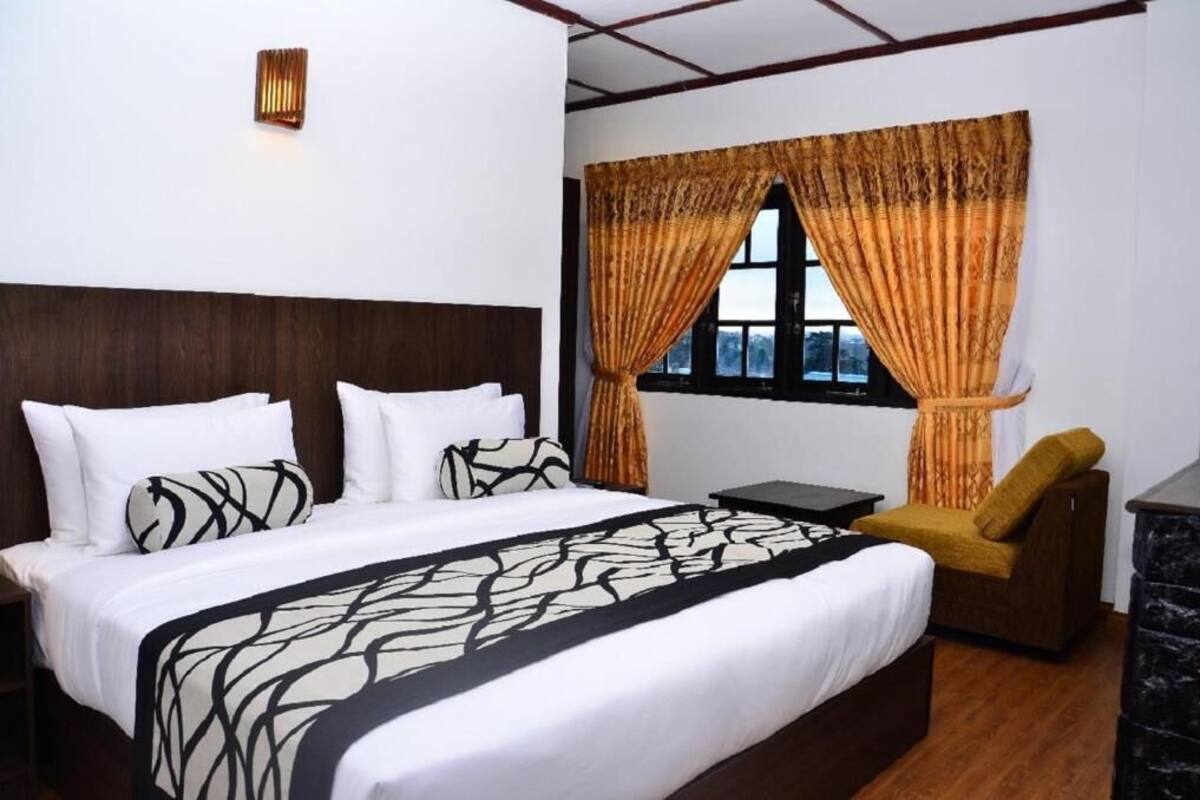 A hotel room with a large bed, a small table, a chair, and a window with curtains.