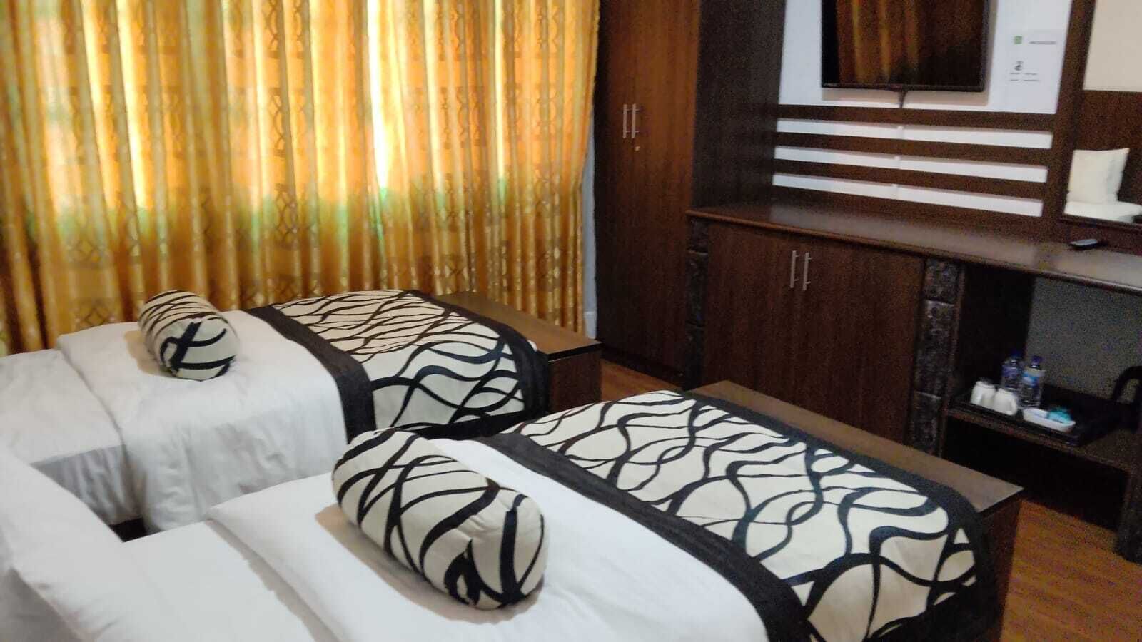 A room with two massage therapy beds, a wooden cabinet, and a television.