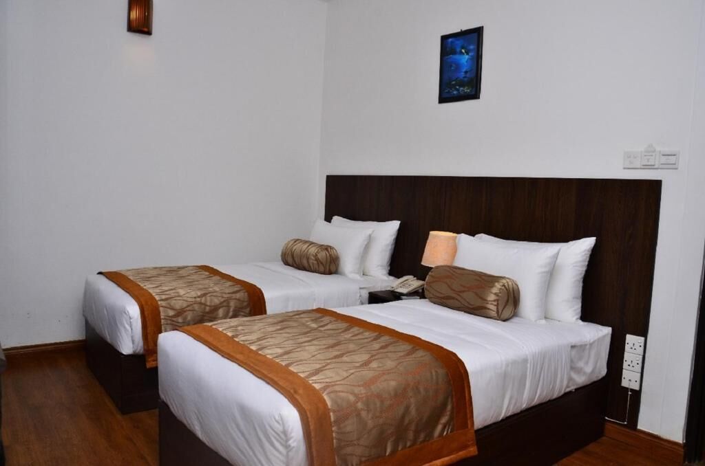 A hotel room with two single beds, a wooden headboard, white bedding, and a small wall-mounted picture.