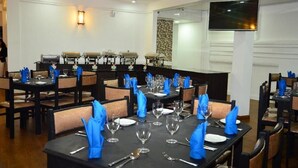 A dining area with tables set for service, a flat-screen TV mounted on the wall, and a buffet line with food warmers. - Nat City Hotel Nuwaraeliya (Nuwaraeliya)