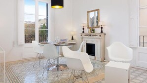 Un comedor con una mesa redonda, sillas blancas, una lámpara colgante negra, una chimenea y vistas a través de grandes ventanales.