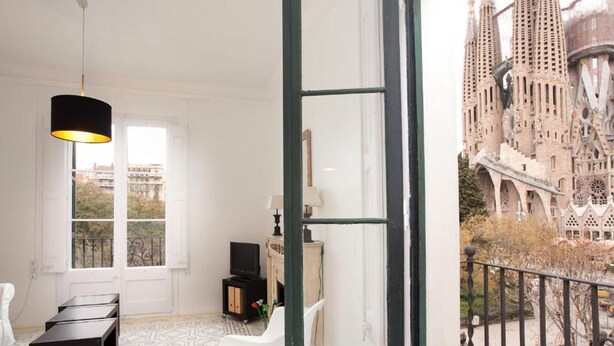 Una habitación con un ventanal grande, una lámpara negra, una silla blanca y una mesita pequeña.