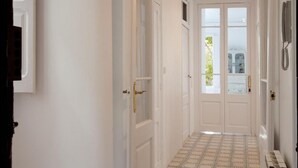 Un pasillo con puertas blancas, piso estampado y vista a zonas verdes al exterior.