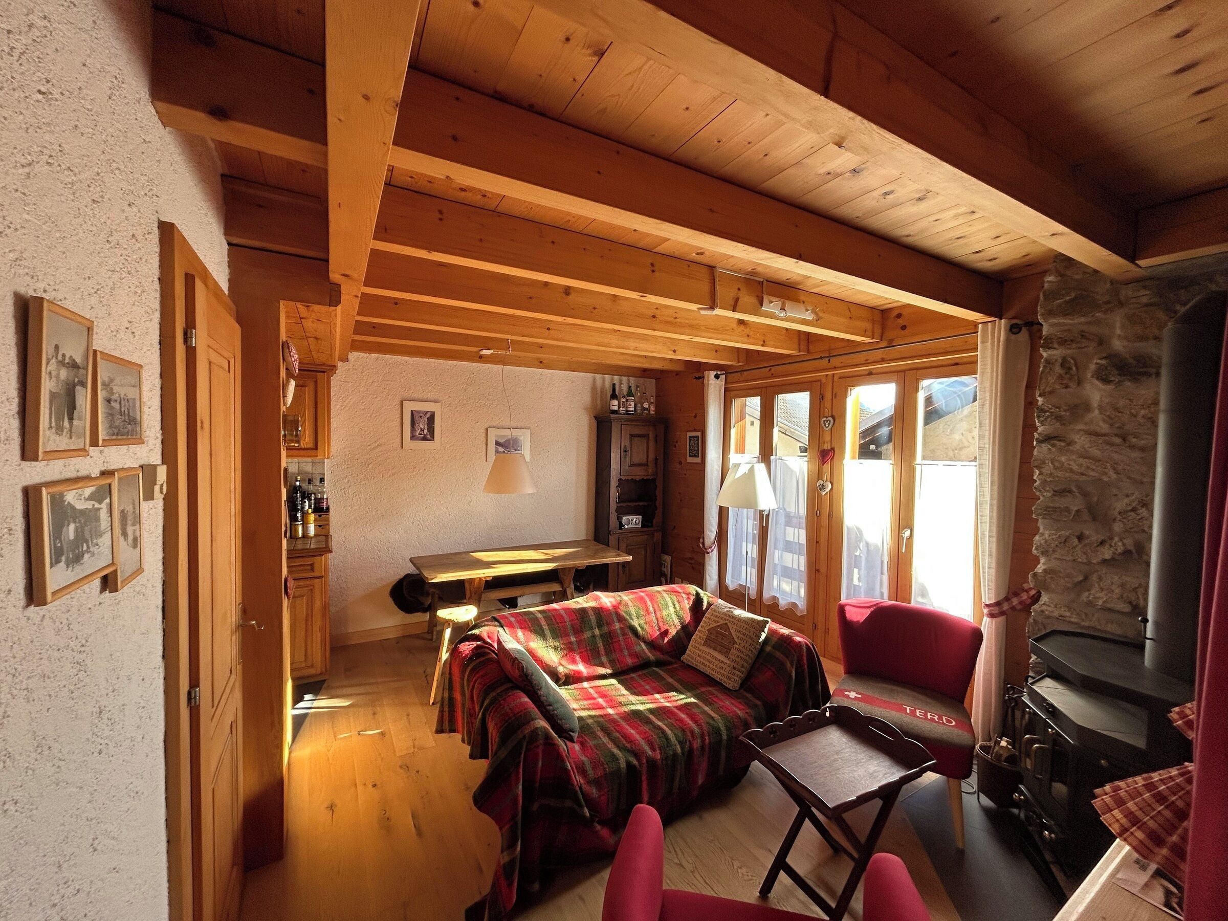 A cozy cabin interior with a wooden ceiling, a dining table, a sofa, and a fireplace.