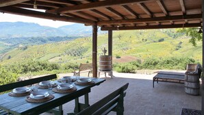 An outdoor dining area with a table set for six, a wooden bench, and a view of a hilly landscape.