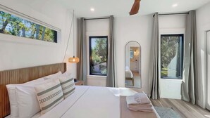 Ein modernes Hotelzimmer mit einem großen Bett, einem Holzkopfschild, einem großen Fenster und Blick ins Freie.