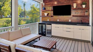 Eine moderne Außenküche mit Holzwand, einem Flachbildfernseher und einem Essbereich mit einer Couch und einem Tisch.