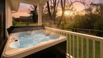 Un jacuzzi en una terraza de madera con vistas a un atardecer y árboles.
