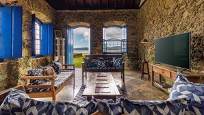 A rustic stone-walled room with a wooden bench, a table, and a television. - Historic house in the center of Paraty, with incredible sea views. (Paraty)